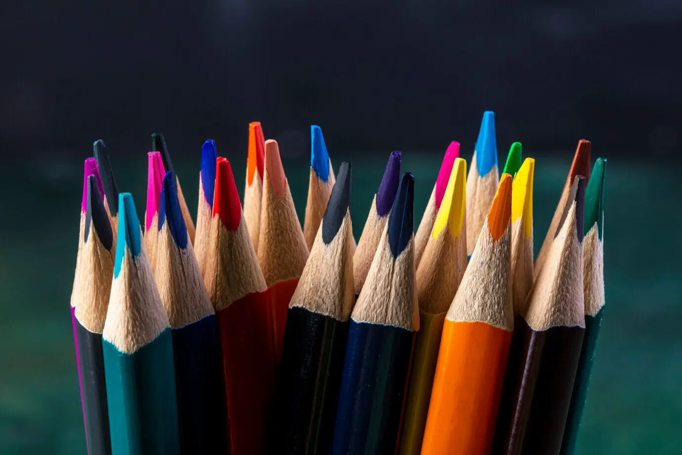 Seitenansicht eines Bündels Buntstifte auf dunklem Untergrund.